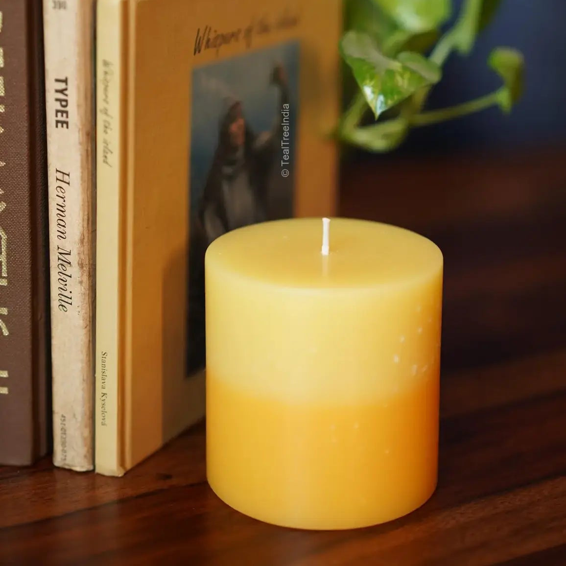 Yellow gradient pillar candle placed with vintage books and green plants – ideal for cozy home decor.