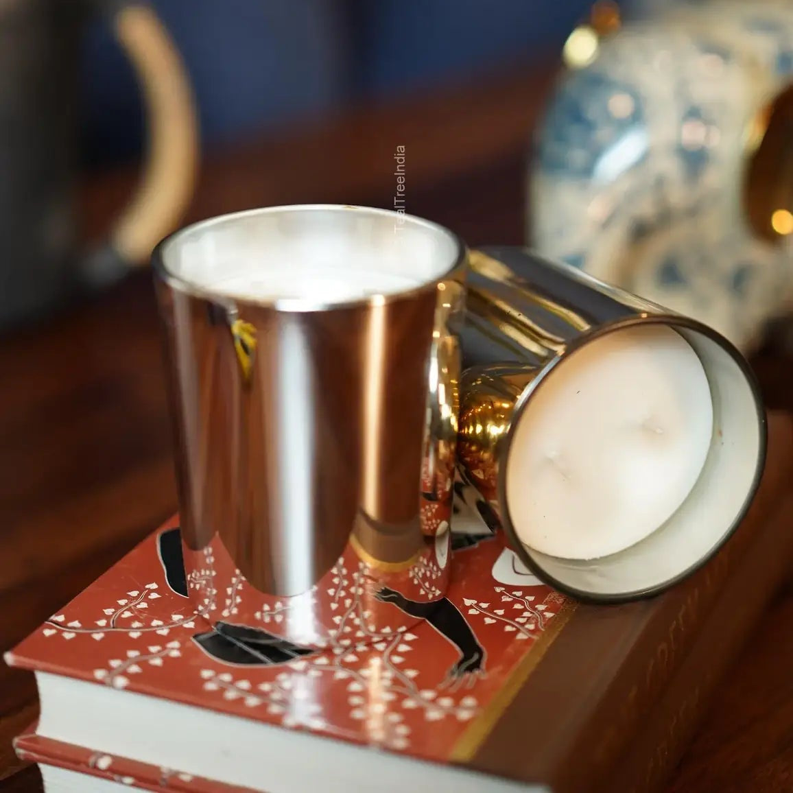 Glossy metallic candle jars with white wax on top of a red illustrated book, styled for premium appeal.